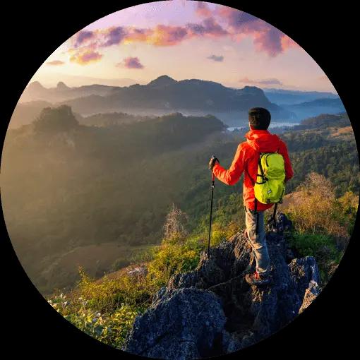 A man looks over a valley and neighboring hills from the top of a mountain.